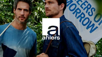 ein Mann hält eine Fahne mit der Aufschrift "Pioneers of Tomorrow" und schaut in die Kamera. Der zweite man mit einem Rucksack schaut in die Ferne.  Im Hintergrund ist grüne Naturhecke. Darüber das Logo des NETFORMIC Kunden Ahlers