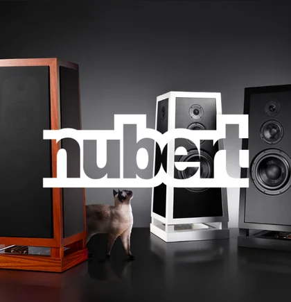 Three high-end Nubert speakers with a light-colored cat walking between them, and the Nubert logo above – representing the NETFORMIC customer case in the D2C segment for premium audio commerce