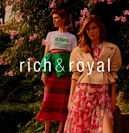 Eine Frau steht Modell in einem Feld. Sie hat modischen Kleidung der Firma Rich & Royal an und schaut zur Seite. Darüber das Logo von NETFORMIC Kunde Rich & Royal.