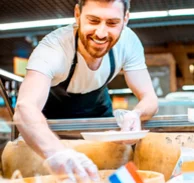 Lächelnder Bäcker greift zu Brot in der Gebäcktheke.