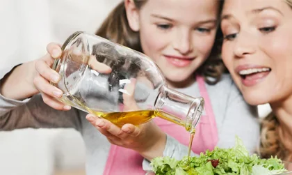 Lächelnde Mutter und Tochter gießen das Olivenöl auf den Salat.