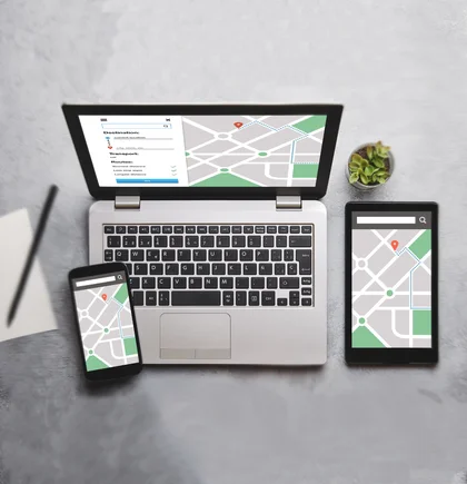 Laptop, Tablet und Handy mit Googlemap-Karte auf den Bildschirmen stehen auf einer grauen Oberfläche. Aufnahme von oben.