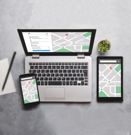 Laptop, Tablet und Handy mit Googlemap-Karte auf den Bildschirmen stehen auf einer grauen Oberfläche. Aufnahme von oben.