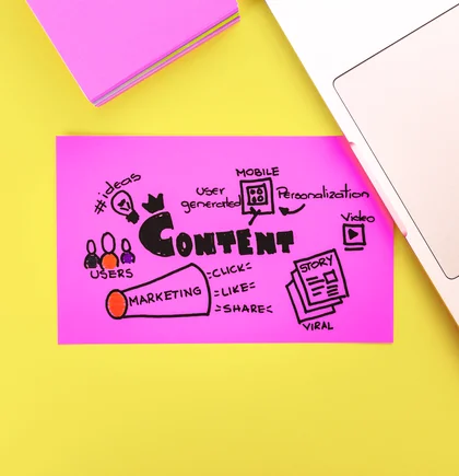 Ein Haftnotizstapel in magenta, ein Haftnotiz in magenta mit aufgeschriebenen Contentplan, ein Teil von Laptoptastatur oben rechts. Gelber Hintergrund.