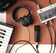 Session Kundencase Ein Headset, ein Mikrofon und ein Digital Piano angeschlossen an einem Tonaufhanmegerät liegen auf dem Tisch.