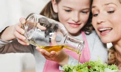 Reformhaus Kundencase Lächelnde Mutter und Tochter gießen das Olivenöl auf den Salat.