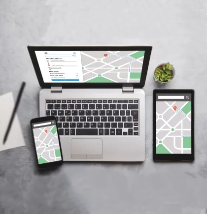 Shopware Beyond Laptop, Tablet und Handy mit Googlemap-Karte auf den Bildschirmen stehen auf einer grauen Oberfläche. Aufnahme von oben.